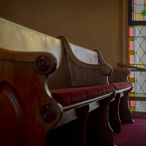 Wooden pews beside a stained-glass window